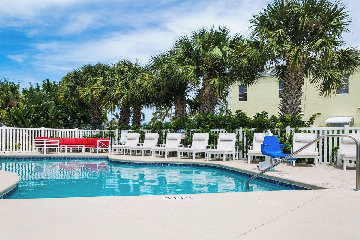 A swimming pool with lounge chairs and a white fence.