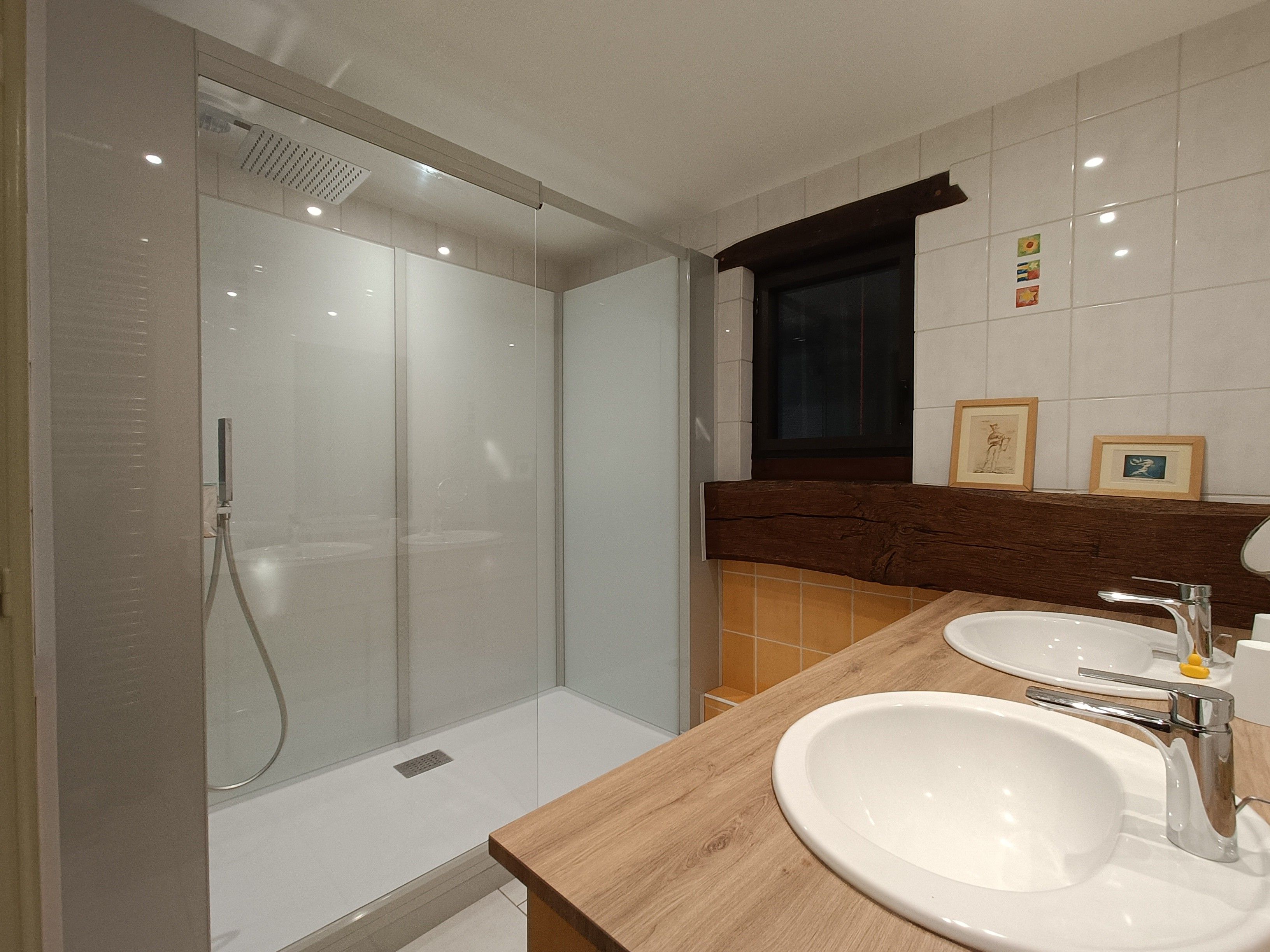 Ein modernes Badezimmer mit einer gläsernen Duschkabine, zwei Waschbecken und einer Holzanrichte.
