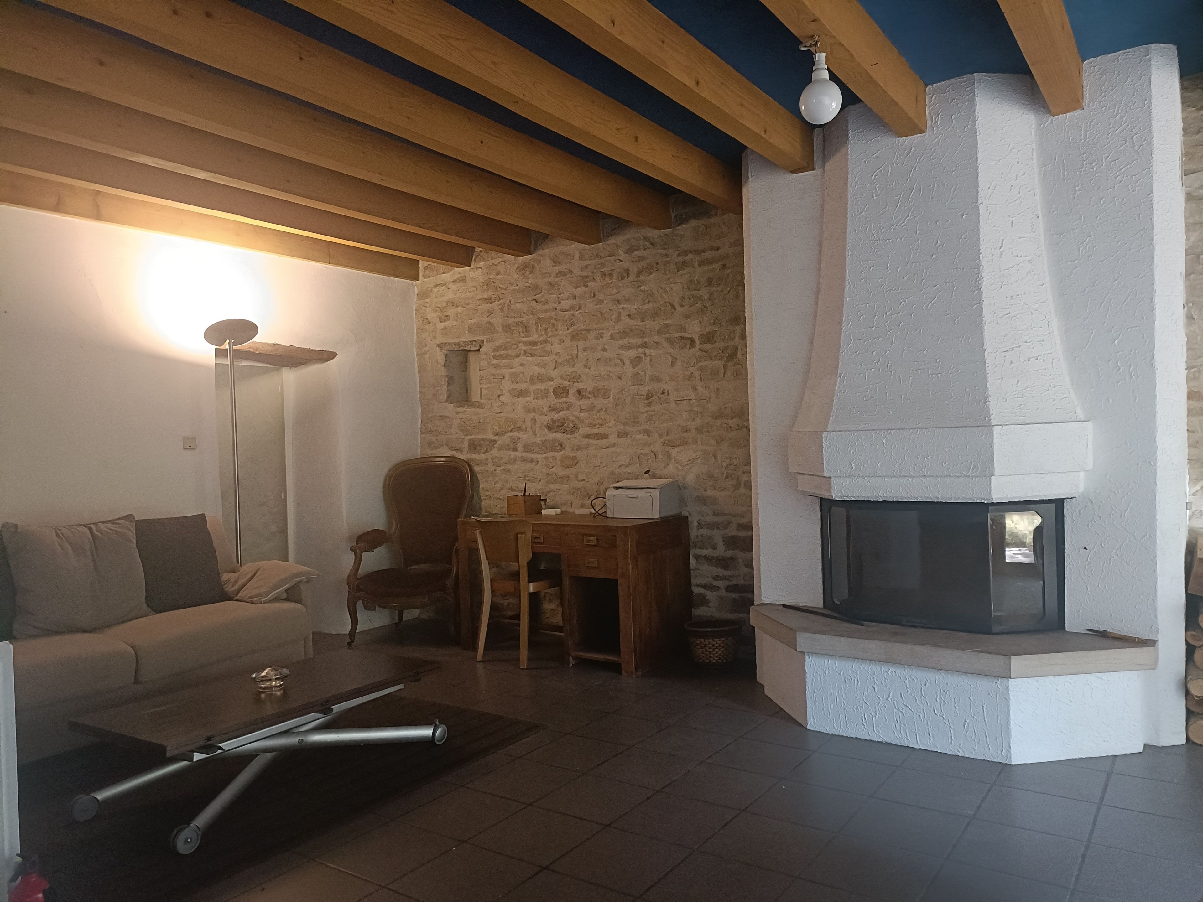 Een gezellige woonkamer met een stenen muur, een open haard, een bank, een salontafel en een lamp.