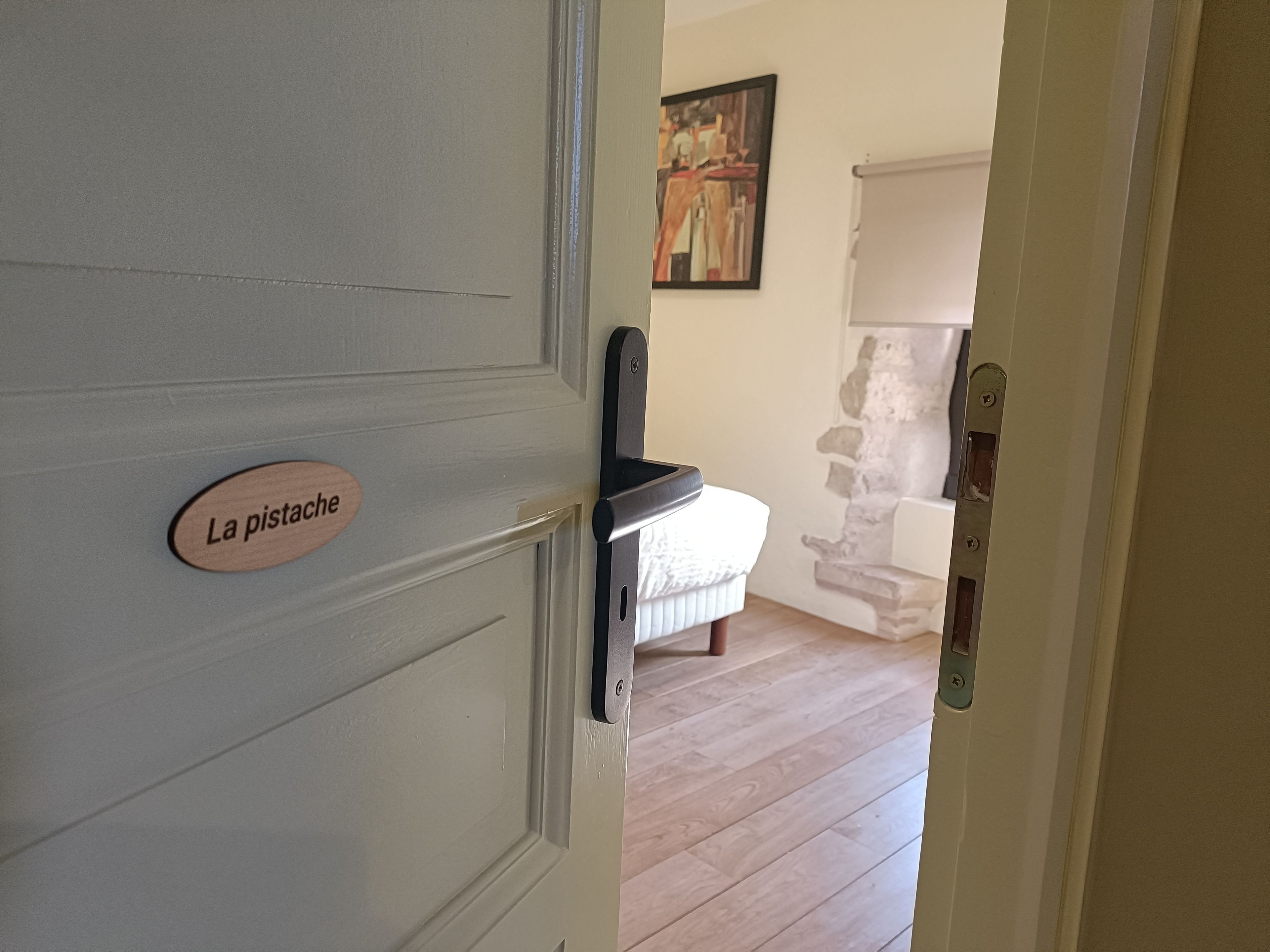 A door with a sign reading 'La pistache,' leading to a room with a bed and a stone wall.