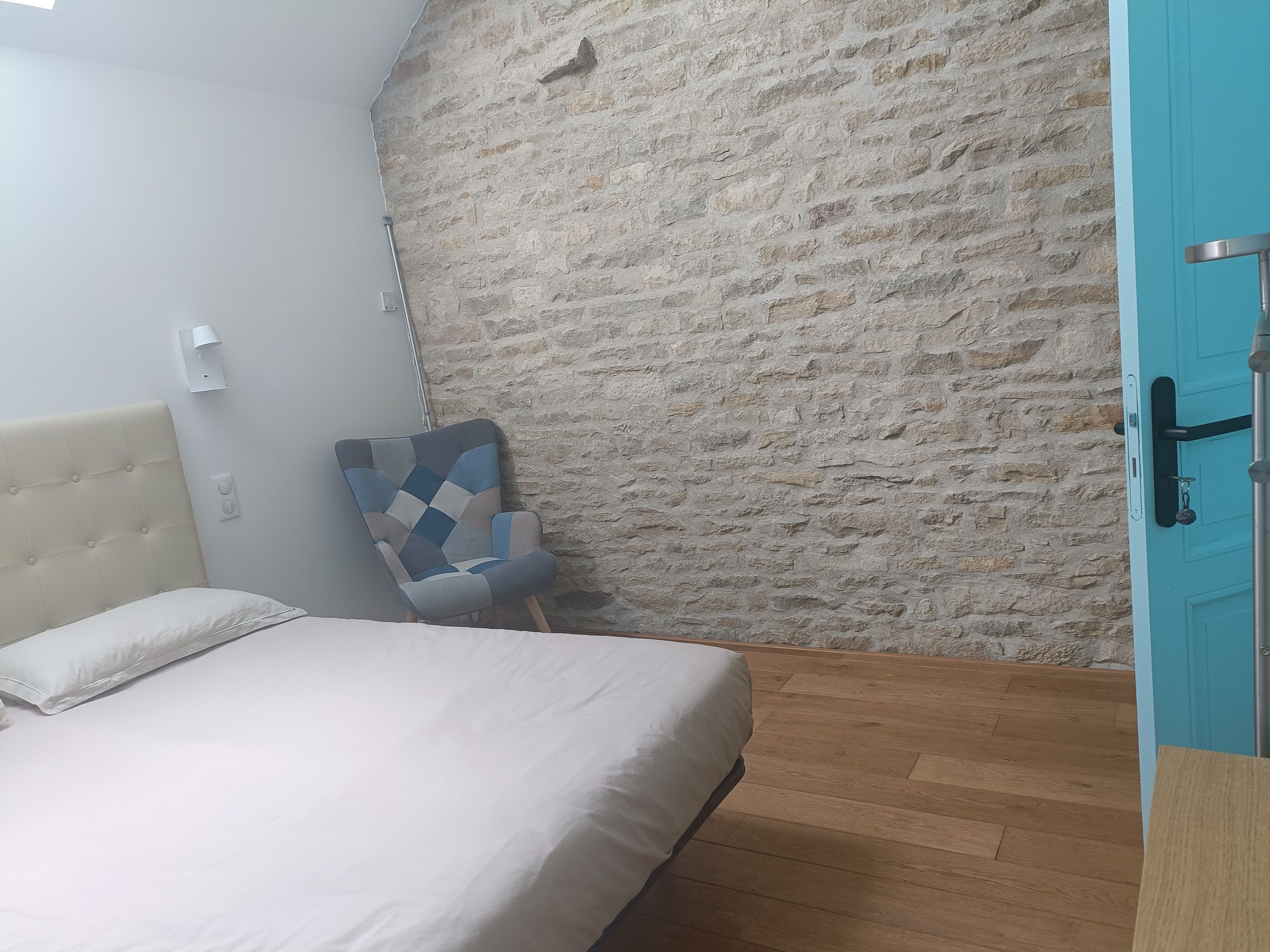A bedroom with a bed, a chair, a stone wall, and a blue door.