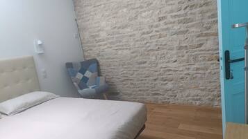 A bedroom with a bed, a chair, a stone wall, and a blue door.