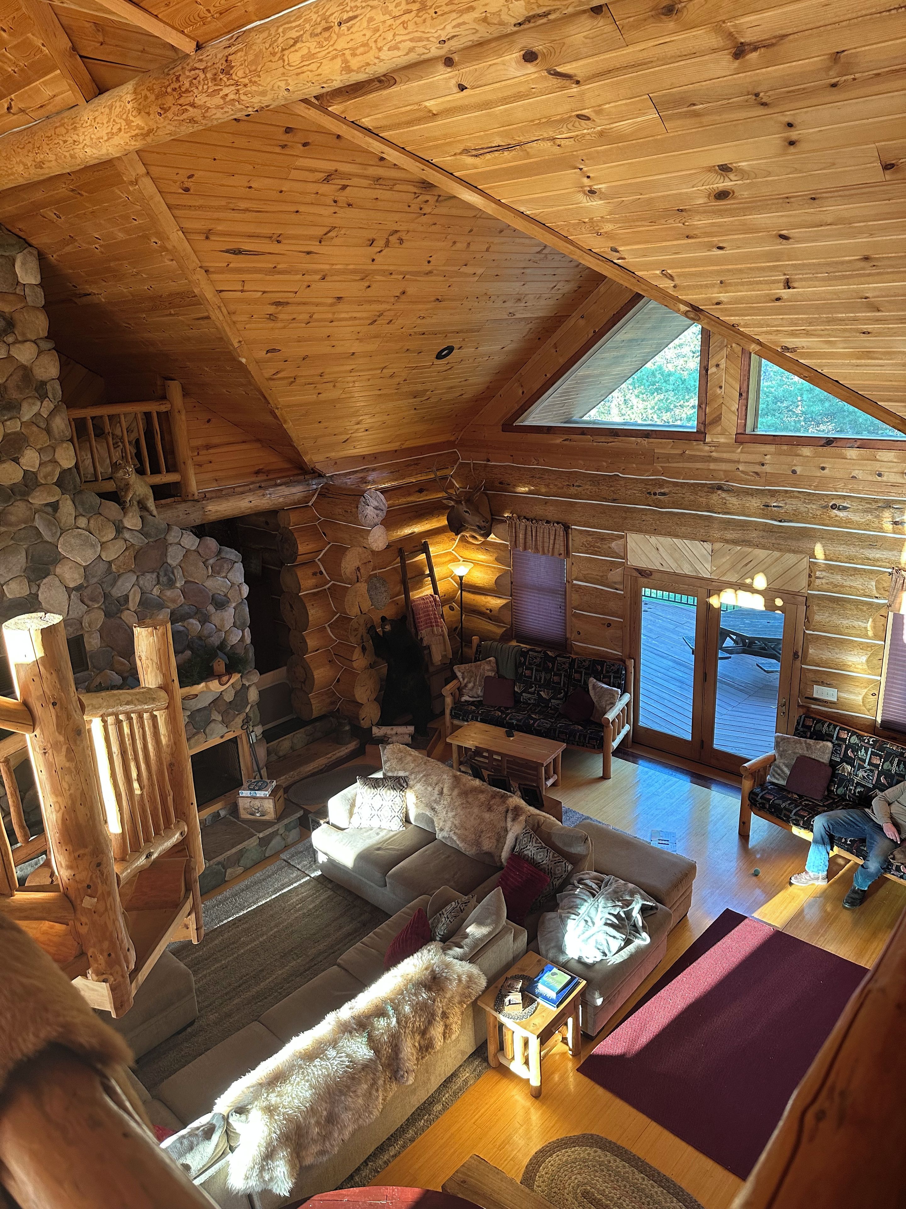 A log cabin interior with a stone fireplace, wooden furniture, and a large dog.
