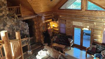 A log cabin interior with a stone fireplace, wooden furniture, and a large dog.