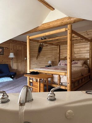 Un dormitorio de cabaña de madera con cama con dosel, una mesita pequeña y un lavamanos con agua corriente.