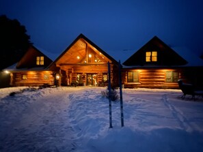 Suuri kuisti ja lumipeitteinen maa – tässä on viehättävä hirsihökkelö.