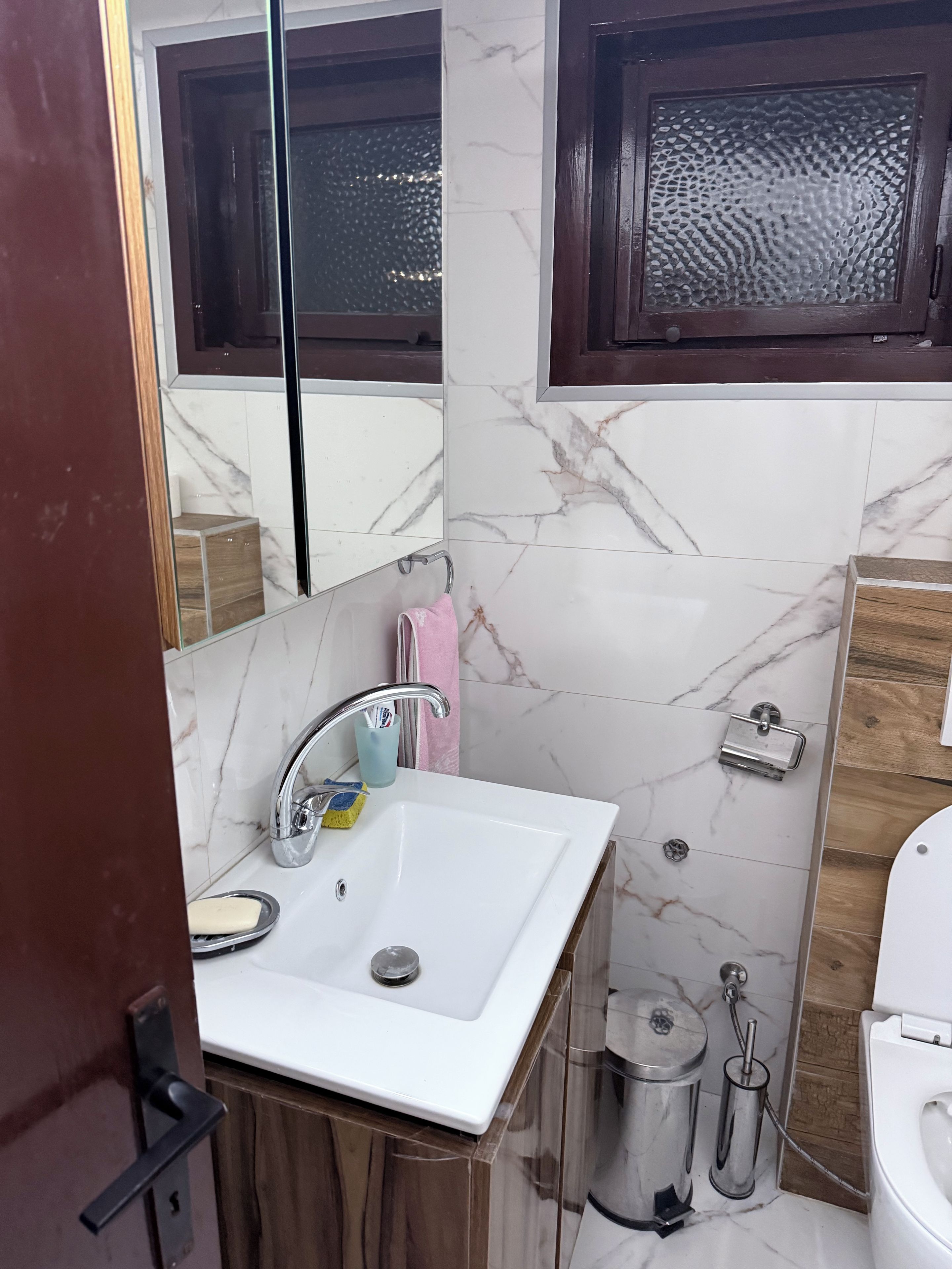 A bathroom with a white sink, a mirror, a wooden cabinet, and a toilet.