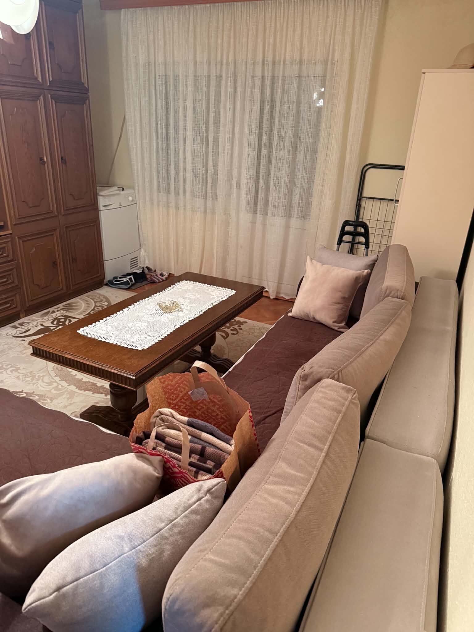 A living room with a sofa, a coffee table with a lace table runner, a patterned rug, and a wooden cabinet.
