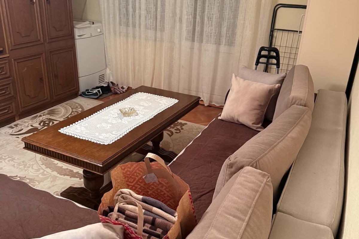 Una sala de estar con sofá, una mesa de centro con camino de encaje, alfombra estampada y un mueble de madera.