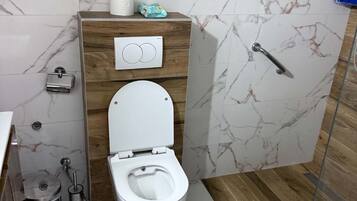 A bathroom with a toilet, a bidet, a toilet paper holder, and a hand dryer.