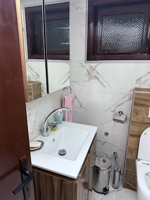 Un baño con un lavamanos blanco, un espejo, una ventana y un inodoro.