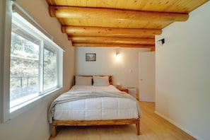 A bedroom with a wooden bed, a window, a painting, and a nightstand. - Cozy Prescott Cabin, Surrounded By Ponderosa Pines (Prescott)