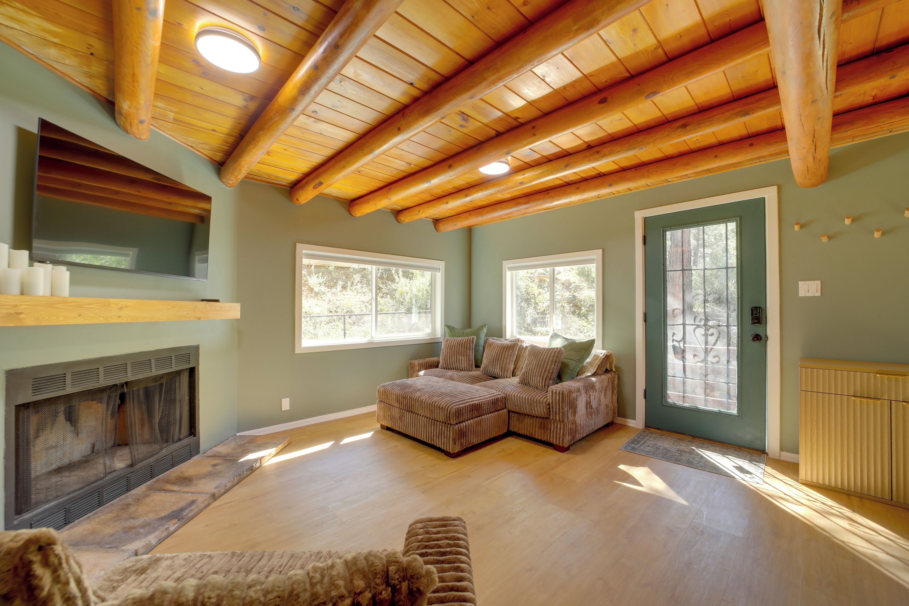 A spacious living room with a high wooden ceiling, a fireplace, a sectional sofa, and large windows.