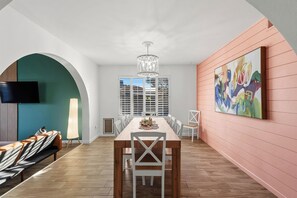A dining area with a long table, chairs, a chandelier, and a large abstract painting on the wall. - Private Pool > Putting Green > GameRoom > Fire Pit > Outdoor Movies (Mesa)