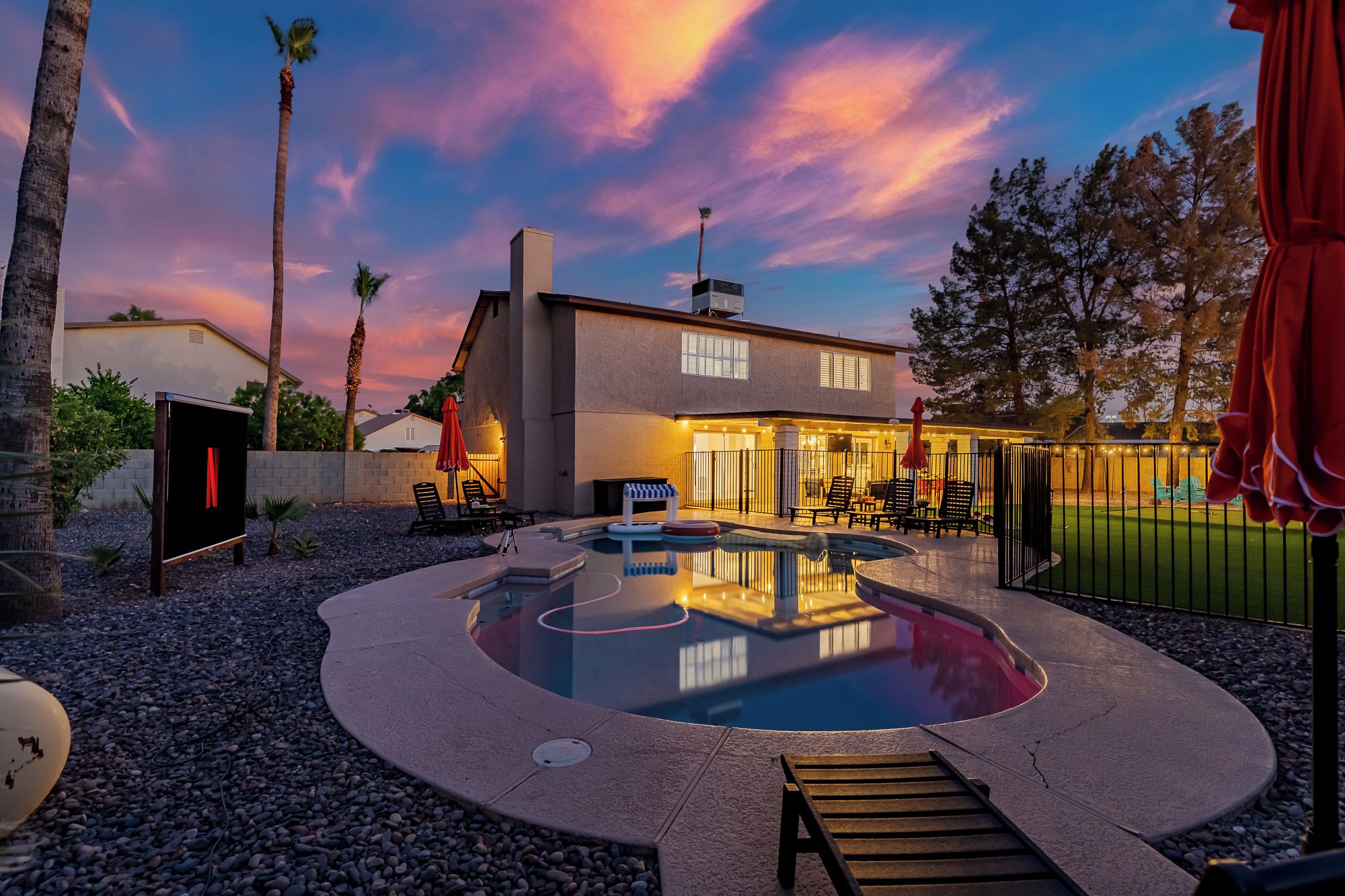 Une maison avec une piscine, un espace extérieur aménagé pour s’asseoir et une terrasse bien éclairée.