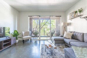 A modern living room with a grey sofa, a coffee table, and a television on a wooden stand. There are two chairs, a potted plant, and a floor lamp. - Central District Condo Seattle Queen Bed Rooftop (Seattle)