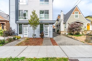 A modern two-story residential building with a central entrance, a small tree in the front yard, and a paved driveway. - North Seattle Townhome Zoo Rooftop Views (Seattle)