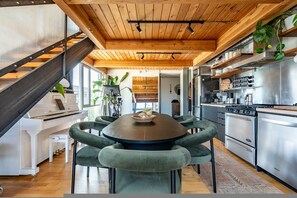 A modern kitchen with a stainless steel stove, a dining area with a round table and green upholstered chairs, and a wooden ceiling with exposed beams. - Loft Apartment Cali King Peloton Walkable (Seattle)