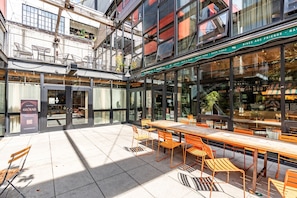 An outdoor seating area with tables and chairs, a storefront with a sign, and a building with multiple stories and balconies. - Loft Apartment Cali King Peloton Walkable (Seattle)