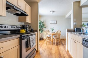 A modern kitchen with wooden cabinets, a stove, and a dining area with a table and chairs. - Centrally Located 1 Bedroom (Seattle)