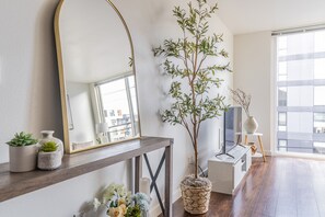A modern living room with a large mirror, a potted plant, a console table with decorative items, a television, and a view of the city through large windows. - Seattle s Modern and Stylish Penthouse Apartment- Wifi Pet Friendly Rooftop (Seattle)