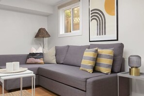 Un salon moderne avec un canapé gris, une petite table d’appoint blanche et un lampadaire.