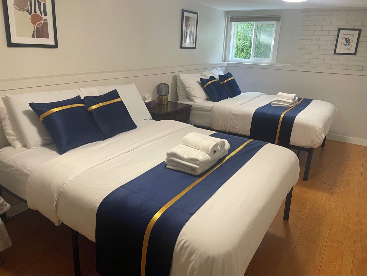Une chambre d’hôtel avec deux lits, chacun agrémenté de draps blancs et de touches de bleu, une table de chevet avec une lampe et une fenêtre donnant sur un paysage verdoyant.