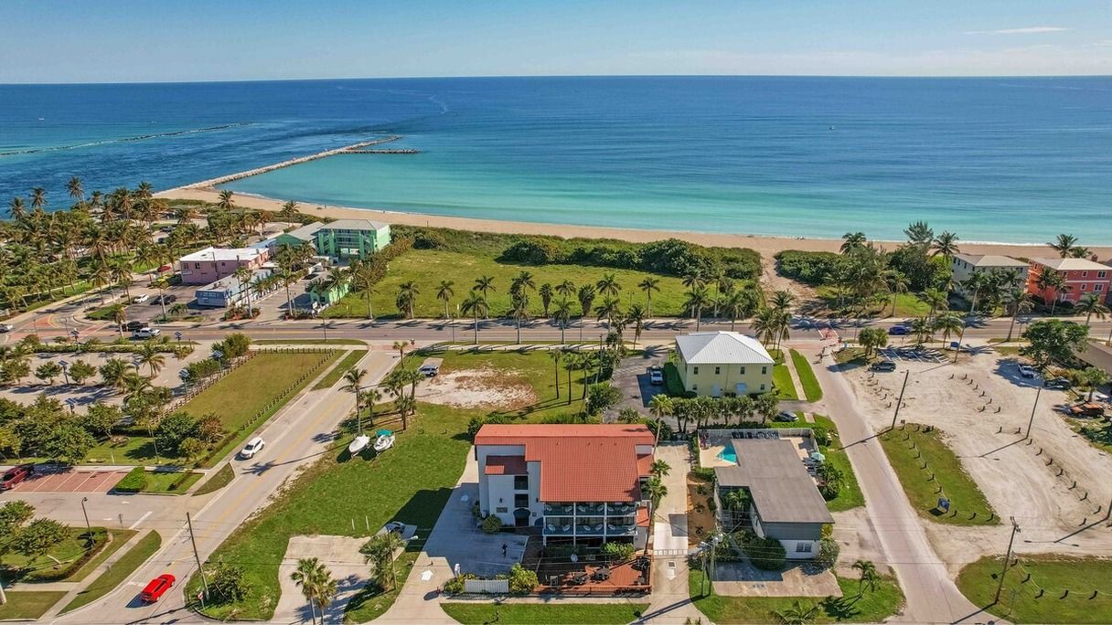 An aerial view of a coastal area with a beach, palm trees, and buildings.
