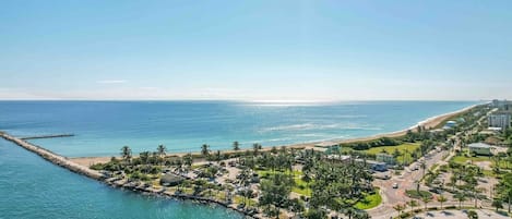 Un resort costero con playa, palmeras y un puerto deportivo.