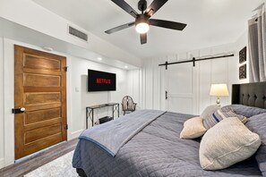 Een slaapkamer met een bed, een aan de muur bevestigde televisie, een plafondventilator en een houten deur.