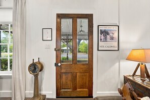Een houten deur met een ruit, een ingelijst certificaat aan de muur, een antieke klok en een lamp op een houten tafel.