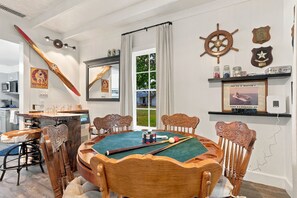 A room with a pool table, wooden chairs, a bar stool, a wooden spoon, a framed picture, and a shelf with decorative items. - Walter-Jenschke Sunday House - Bumper Pool Table (Fredericksburg)