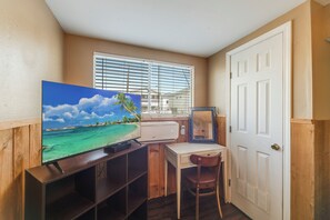 A small room with a television displaying a tropical beach scene, a desk with a chair, and a door. - BC8--Studio Sleeps 2 Adults/2 Kids, Walk to Beach, Pool/Hot Tub, Dogs OK! (Port Aransas)