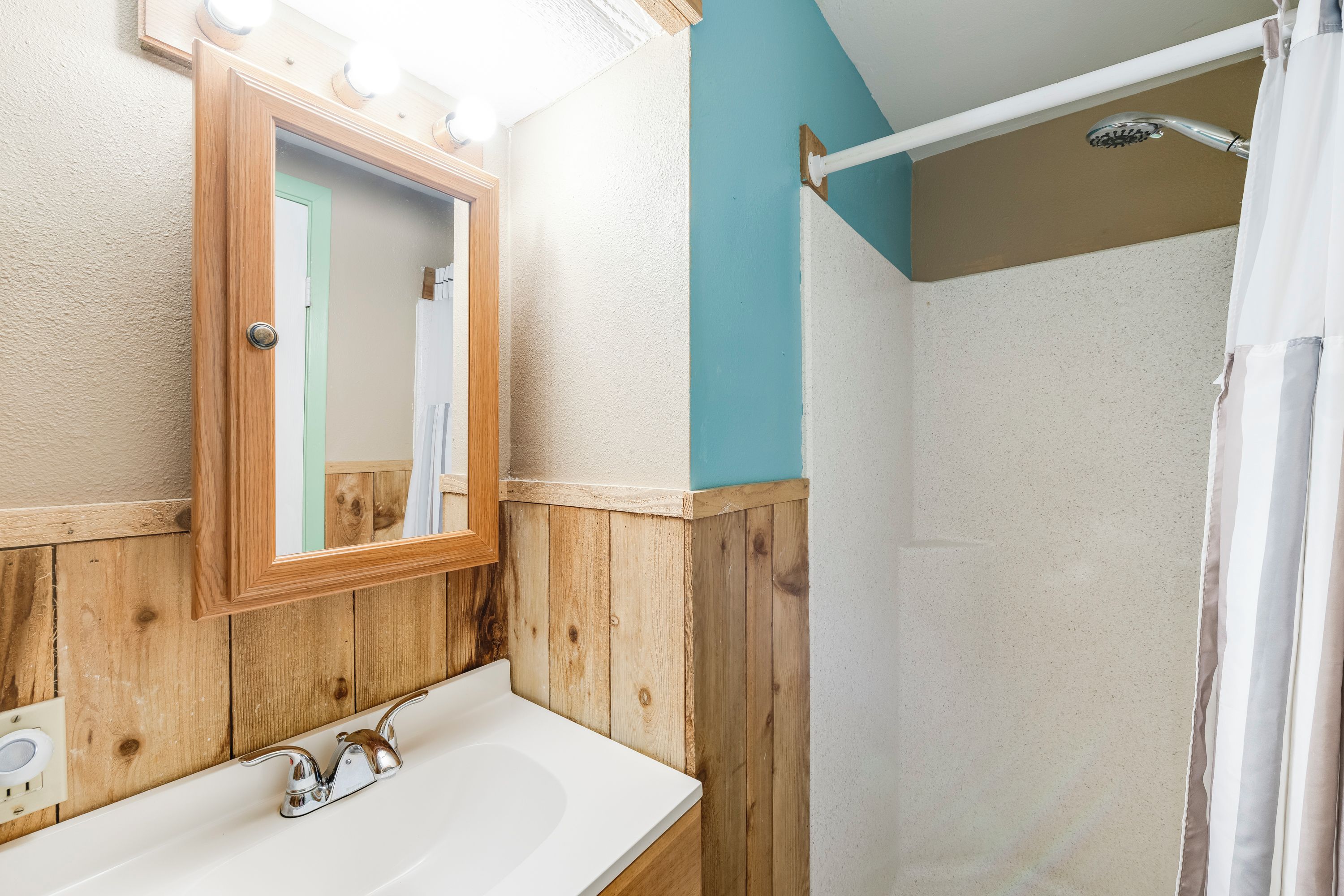 A bathroom with a wooden vanity, a mirror, and a shower area.
