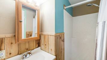 A bathroom with a wooden vanity, a mirror, and a shower area.