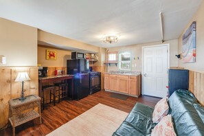 A compact kitchen with a refrigerator, microwave, and stove, wooden cabinets, a small dining area with stools, and a living room with a sofa and a rug. - BC8--Studio Sleeps 2 Adults/2 Kids, Walk to Beach, Pool/Hot Tub, Dogs OK! (Port Aransas)