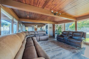 A spacious living room with a large sectional sofa, a smaller sofa, and a coffee table. The room has a wooden ceiling and large windows providing natural light. - New Listing in Eugene's highly sought after "Ferry Street Bridge" neighborhood. (Eugene)