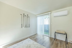 Een kamer met een houten vloer, een witte wand en een schuifdeur naar een achtertuin.