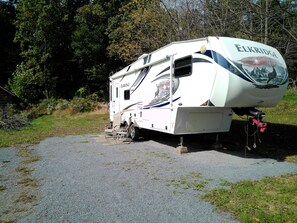 A recreational vehicle (RV) named 'Elk Ridge' parked on a gravel surface with a grassy area and trees in the background.