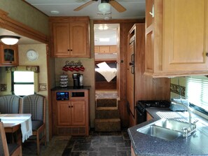 A compact kitchen with wooden cabinets, a coffee station, a sink, and a stove. - Simple stay - Cozy camper (Mohnton)