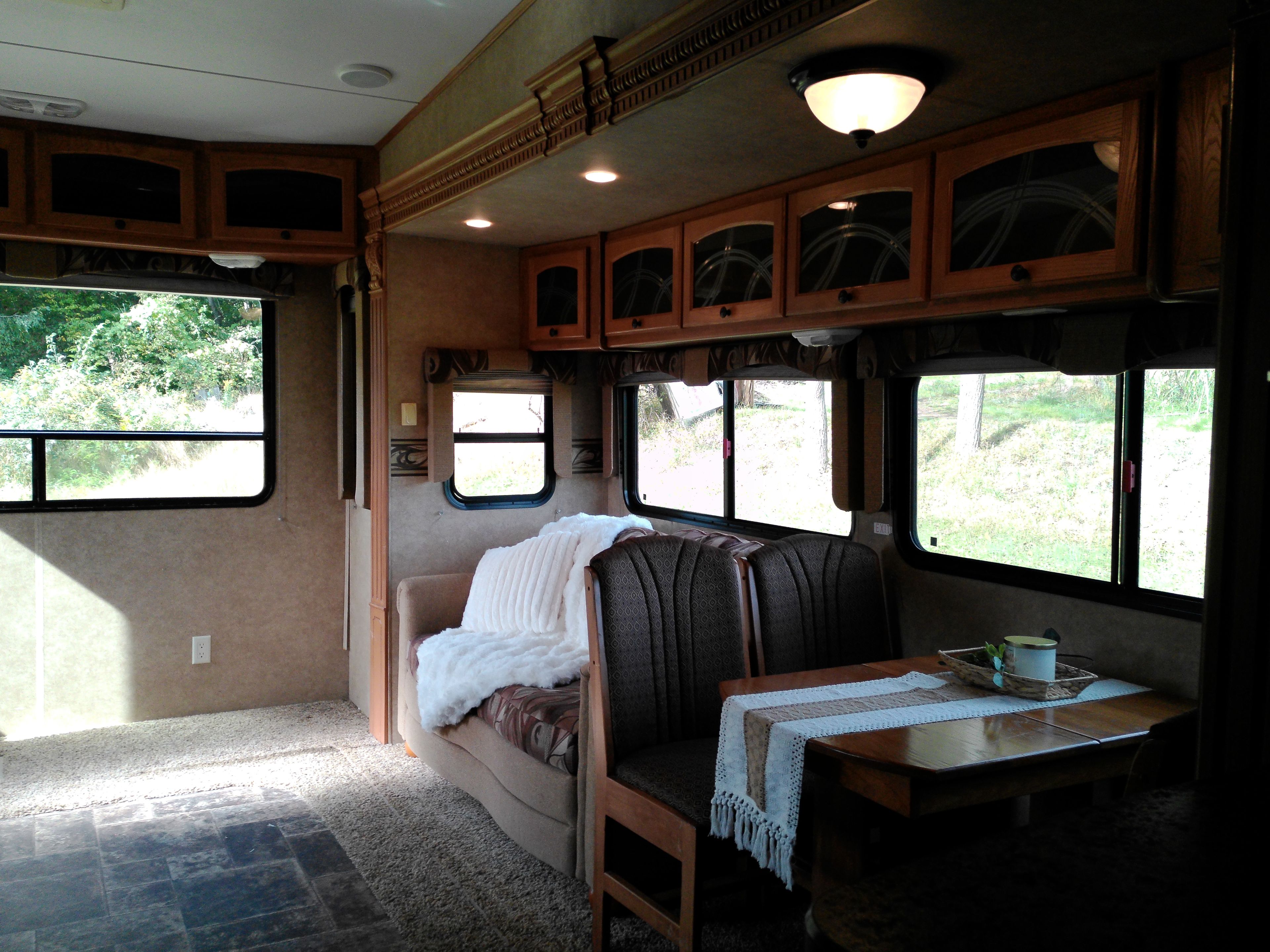 Un interior de caravana acogedor, con zona de estar, una mesa con una taza y ventanas que ofrecen vistas a la vegetación.