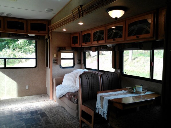 A cozy RV interior with a seating area, a table with a cup, and windows providing views of greenery.