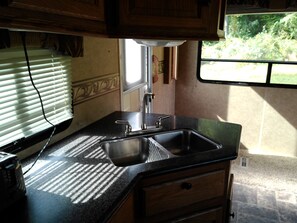 A kitchen with a sink, countertop, and wooden cabinets. - Simple stay - Cozy camper (Mohnton)