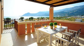Ein Balkon mit Tisch für zwei Personen, mit Blick auf eine reizvolle Berg- und Wasserlandschaft.