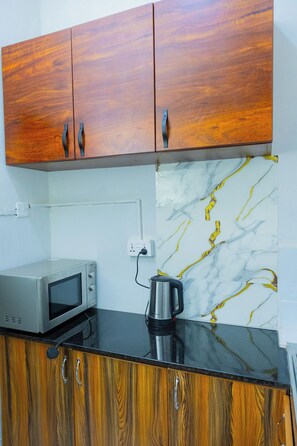 A kitchenette with wooden cabinets, a microwave, a kettle, and a marble backsplash. - Bethel Residence; Private 1-bedroom home in Kampala-free WiFI, Netflix, parking (Kampala)