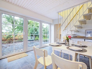 A dining area with a table set for two, a staircase, and a view of a garden through large glass doors. - Holiday Apartment With 1 Bedroom (Westerdeichstrich)