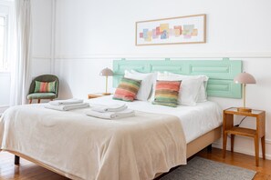 Un lit bien fait, avec du linge de lit blanc et des oreillers à rayures, une tête de lit verte et deux tables de chevet avec des lampes.