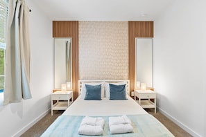 A hotel room with a bed, two bedside tables, a nightstand, a window with curtains, and a wall-mounted mirror. - 3BR Near Disney, Harry Potter and Mickey Rooms (Four Corners)