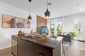 A modern kitchen with a central island, pendant lighting, and a large window overlooking a garden. - 3BR Near Disney, Harry Potter and Mickey Rooms (Four Corners)