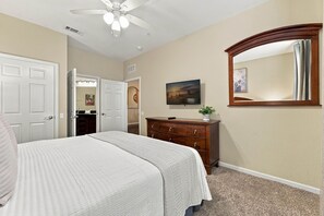 Une chambre à coucher comprenant un lit, une commode, un ventilateur de plafond, un téléviseur et un miroir.
